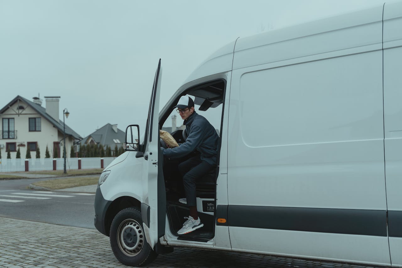 about-us Courier delivering a package from a van in suburban neighborhood, showcasing logistics and last-mile delivery services.